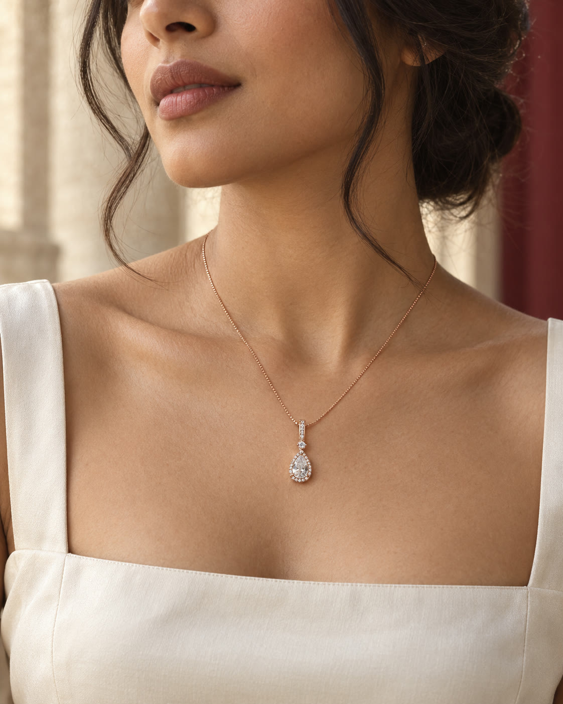 A rose-tone pear halo pendant necklace worn close at the neckline